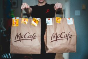 A person holds two McCafé food delivery bags indoors, emphasizing fast food service.